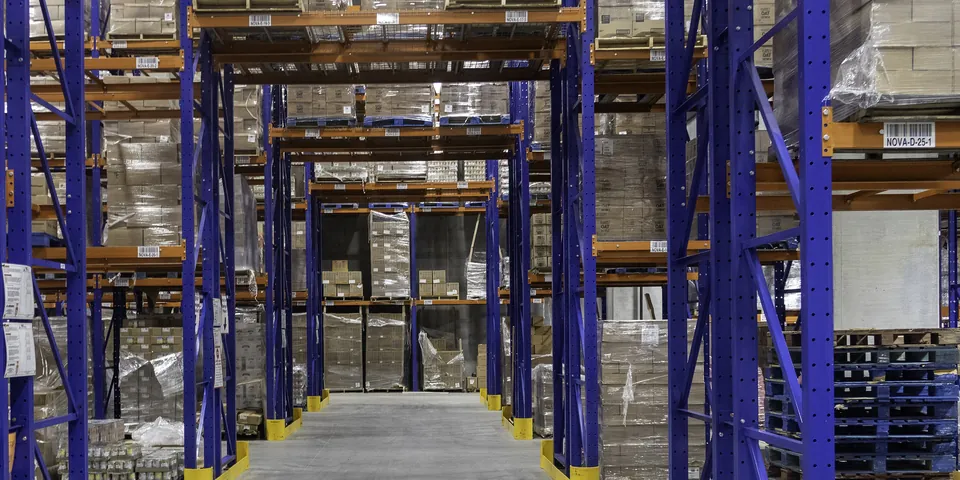 Allée d’un entrepôt de stockage, palettes de cartons filmées sur des racks